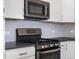 Up close shot of range and microwave, highlighting the tile backsplash and white cabinetry at 3654 Penang Dr, Castle Rock, CO 80109