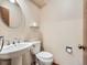 Charming half-bathroom featuring a pedestal sink, toilet, and a round decorative mirror at 6141 W Evans Pl, Lakewood, CO 80227