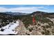 Aerial view of a wooded property with a house indicated by a red arrow, mountains in distance at 24860 N Mountain Park Dr, Evergreen, CO 80439