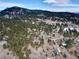 Aerial view of a wooded property with a house, driveways, and surrounding mountains at 24860 N Mountain Park Dr, Evergreen, CO 80439