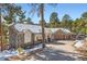 A beautiful exterior view, with a stone finish and a three-car garage, all surrounded by natural forest and light snow at 24860 N Mountain Park Dr, Evergreen, CO 80439