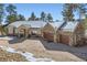 Stunning home with a stone finish and a three-car garage, accented by mature trees, with light snow along the driveway at 24860 N Mountain Park Dr, Evergreen, CO 80439