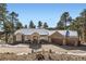 Charming stone home with a driveway that leads to a three-car garage, nestled amongst mature trees, with a roof dusted in snow at 24860 N Mountain Park Dr, Evergreen, CO 80439