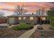 Charming brick home featuring a manicured front yard and covered entry, set against a vibrant sunset sky at 5540 E Jewell Ave, Denver, CO 80222