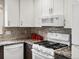 Close-up of kitchen with gas range, white cabinetry, and mosaic tile backsplash at 5261 S Malta Way, Centennial, CO 80015