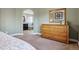 Bright bedroom featuring a wooden dresser, carpet flooring, and an open doorway to the ensuite bathroom at 1300 W 13Th Ave, Broomfield, CO 80020