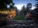 Backyard view features a patio with fire pit, outdoor dining set, lush lawn, mature trees, string lights, and landscaping at 7264 Wembley Pl, Castle Pines, CO 80108