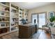 Home office featuring built-in bookshelves, a large wooden desk, and a comfortable chair with outdoor access at 9880 E Progress Cir, Greenwood Village, CO 80111
