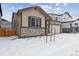 Tan house with stone accents, a two-car garage, and landscaping; winter scene at 144 Wooten Ave, Brighton, CO 80601