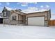 Tan house with stone accents, a two-car garage, and landscaping; winter scene at 144 Wooten Ave, Brighton, CO 80601