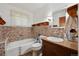 Bathroom featuring a white tub, brown accent tiles, wood cabinets and a window with sheer curtains at 675 Holland St, Lakewood, CO 80215