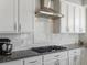 Modern kitchen with white cabinets, granite countertops, stainless steel hood, and gas stovetop at 2755 Geneva St, Denver, CO 80238