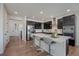 Open kitchen with a center island, dark cabinetry, stainless steel appliances, and hardwood floors, adjacent to the hallway at 6802 S Uriah St, Aurora, CO 80016
