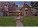 Charming two-story brick home with lush green lawn at dusk with the interior aglow at 239 Ash St, Denver, CO 80220