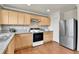 Well-lit kitchen with stainless steel refrigerator, white appliances, wood cabinets, and tiled backsplash at 21455 E 44Th Ave, Denver, CO 80249