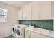 Bright laundry room with white cabinets, white machines, a countertop sink, and a decorative green backsplash at 13838 Honey Hush Trl, Parker, CO 80134