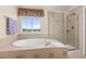 A luxurious bathroom features a soaking tub under a picture window and a separate glass-enclosed shower at 16120 E 119Th Ave, Commerce City, CO 80022
