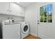 Bright laundry room with wood floors, washer, dryer, white cabinets, and a door to the outside at 3884 S Niagara Way, Denver, CO 80237