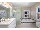 Bright bathroom features a double sink vanity, walk-in glass shower, and a soaking tub with natural light from two windows at 1827 N Bellaire St, Denver, CO 80220