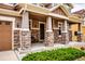 Inviting front porch of a two-story home, featuring stone pillars, recessed lighting, and a dark-stained front door at 3421 E 143Rd Dr, Thornton, CO 80602
