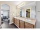 Dual sink bathroom with wood cabinets, bright lighting, and doorway to the walk-in closet at 3745 Balderas St, Brighton, CO 80601