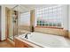 A modern bathroom with a glass enclosed shower and a soaking tub set beneath a large glass block window at 641 Briar Haven Dr, Castle Pines, CO 80108