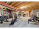 Unfinished basement with exposed wooden ceiling beams, cement walls, and a variety of exercise equipment at 1104 Fieldstone Pl, Highlands Ranch, CO 80126