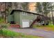 Charming green two-story home with a deck and a garage surrounded by lush trees and a driveway at 5237 S Olive Rd, Evergreen, CO 80439