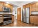 Modern kitchen with stainless steel appliances, wooden cabinets, and hardwood floors at 13516 Thorncreek Cir, Thornton, CO 80241