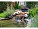Close-up of a serene backyard waterfall flowing into a clear pond amidst vibrant plants and stones at 222 S Olive St, Denver, CO 80230