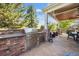 Outdoor kitchen features a stainless steel grill, brick surround, countertop space, and covered patio with a dining set at 10660 Weathersfield Ct, Highlands Ranch, CO 80129