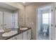 A dual sink bathroom vanity featuring gray cabinets and a doorway to a combined toilet and shower at 2474 Ravenswood Ct, Longmont, CO 80504