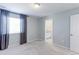 An empty bedroom with neutral walls, carpet, and a window with decorative curtains and a door to the ensuite at 2474 Ravenswood Ct, Longmont, CO 80504