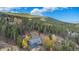 An aerial view of the home surrounded by green trees and mountains with a bright, sunny sky overhead at 779 Aspen Way, Evergreen, CO 80439