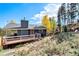 View of rear of home with wood deck, chimney, and view of surrounding landscape with trees and brush at 779 Aspen Way, Evergreen, CO 80439