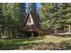 A-frame home with a brown exterior, surrounded by lush trees, featuring a wooden deck and staircase at 100 Aspen Ln, Evergreen, CO 80439