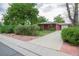 Front yard of cozy brick home with long driveway, mature trees, green bushes and pink decorative rock at 3222 Fenton St, Wheat Ridge, CO 80212