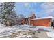 View of the red brick home exterior, driveway with snow, attached two-car garage, and mature trees at 255 Iroquois Dr, Boulder, CO 80303