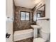 Bathroom features tiled wall, tub and shower, pedestal sink, and a framed mirror at 2220 Quebec St, Denver, CO 80207