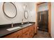 Bright bathroom featuring dual sinks, wood cabinetry, stone flooring, pendant lights, and a glass-enclosed shower at 6016 Stone Creek Dr, Evergreen, CO 80439