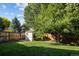 Spacious backyard with lush green lawn, mature trees, a storage shed, and wooden fence at 6073 W Adriatic Pl, Lakewood, CO 80227