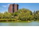 Exterior view of tall brick apartment building next to a lake with mature trees on the property at 480 S Marion Pkwy # 306, Denver, CO 80209