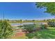 Scenic water view from the property, featuring a white fence, lush greenery, and neighborhood homes in the distance at 293 Wagonwheel Dr, Fort Lupton, CO 80621