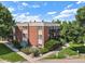 Exterior view of a red brick apartment building with mature trees and green grass at 5995 W Hampden Ave # 18C, Denver, CO 80227