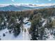 Aerial view of a cozy cabin nestled among pine trees on a snowy landscape with majestic mountains in the distance at 8537 S Doubleheader Hwy, Morrison, CO 80465