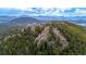 Aerial view of a rocky, tree-covered peak with mountains in the distance under a partly cloudy sky at 8537 S Doubleheader Hwy, Morrison, CO 80465