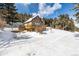 Charming cabin with a wooden deck and snow covered landscape with evergreens and a signpost at 8537 S Doubleheader Hwy, Morrison, CO 80465