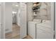 Bright laundry room with washer, dryer, and shelving with paint and bathroom partially visible beyond door at 3251 N Madison St, Denver, CO 80205