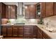 Close-up of the kitchen featuring dark wood cabinetry, tile backsplash, and stainless steel vent hood and gas range at 15392 W 49Th Ave, Golden, CO 80403