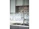 Close-up of the kitchen sink with a patterned tile backsplash and gray cabinets at 3202 S Dahlia St, Denver, CO 80222